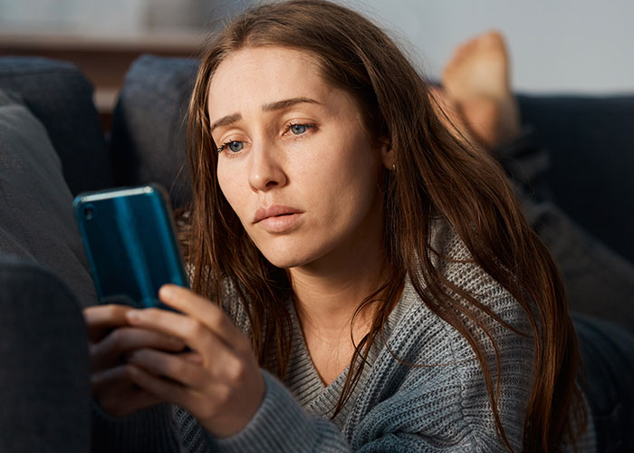 Woman looking suspicious and confused while checking phone during husband's surgery at home on the couch. Woman looking suspicious and confused while checking phone during husband's surgery at home on the couch.