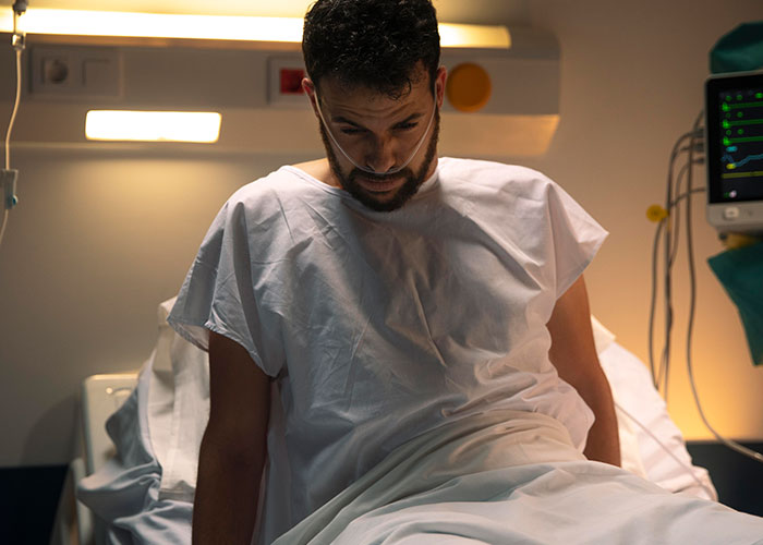 Man in hospital gown sitting on bed, appearing worried during surgery, reflecting suspicion and confusion of wife checking phone. Man in hospital gown sitting on bed, appearing worried during surgery, reflecting suspicion and confusion of wife checking phone.