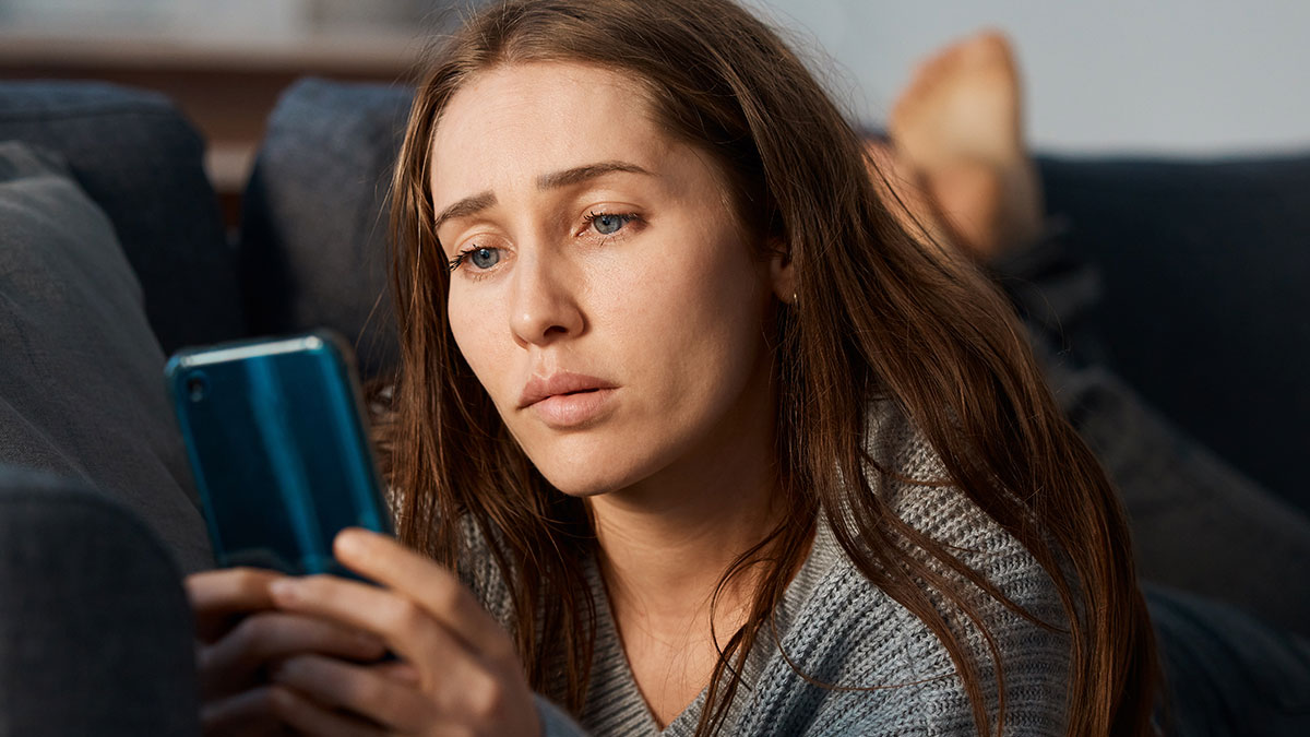 Woman looking suspicious and confused while checking husband's phone during surgery, lying on a couch indoors.