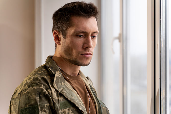 Man in camouflage jacket looking thoughtful by a window, reflecting on husband expects wife work study full time two kids. Man in camouflage jacket looking thoughtful by a window, reflecting on husband expects wife work study full time two kids.