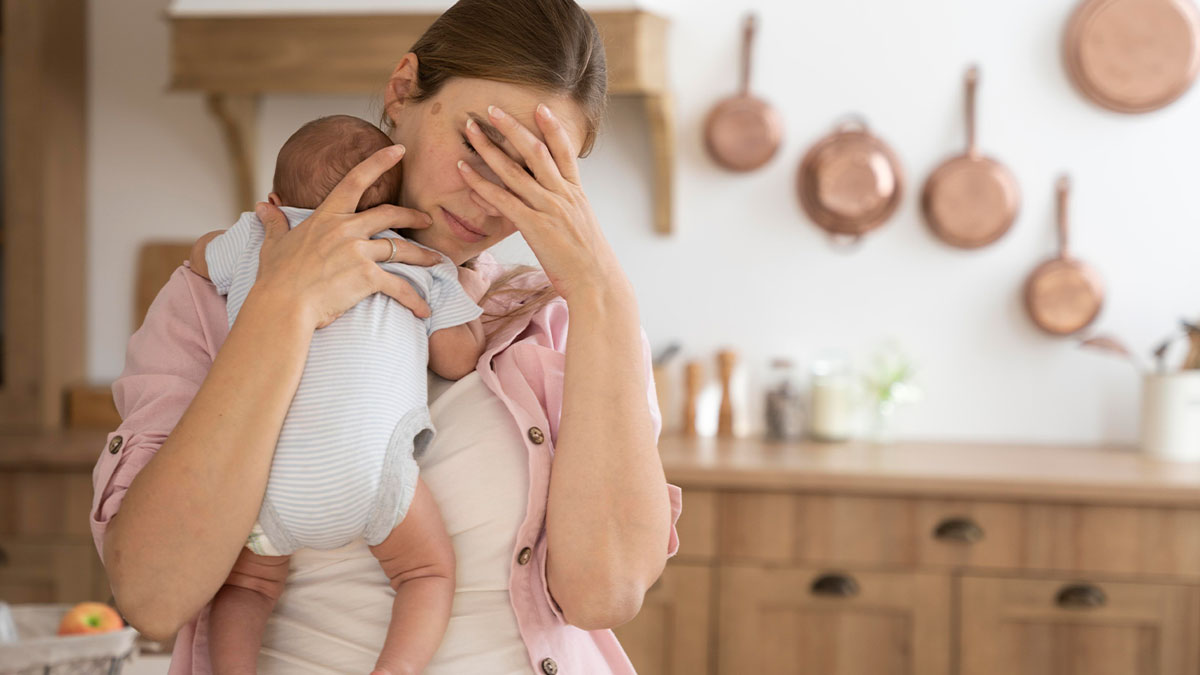 Stressed woman holding baby in kitchen, illustrating husband coercing wife into pregnancy as punishment for cheating.