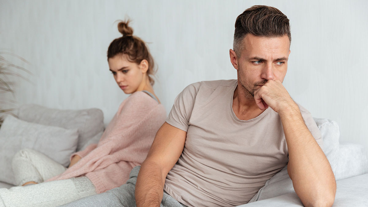 Couple sitting apart on couch looking upset, reflecting tension around intimacy boundaries and potential divorce risk.