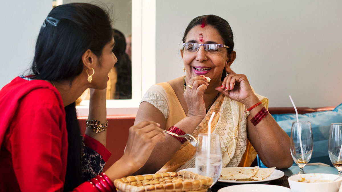 Two women enjoying a meal together, smiling and sharing stories about husband parents native language and culture.