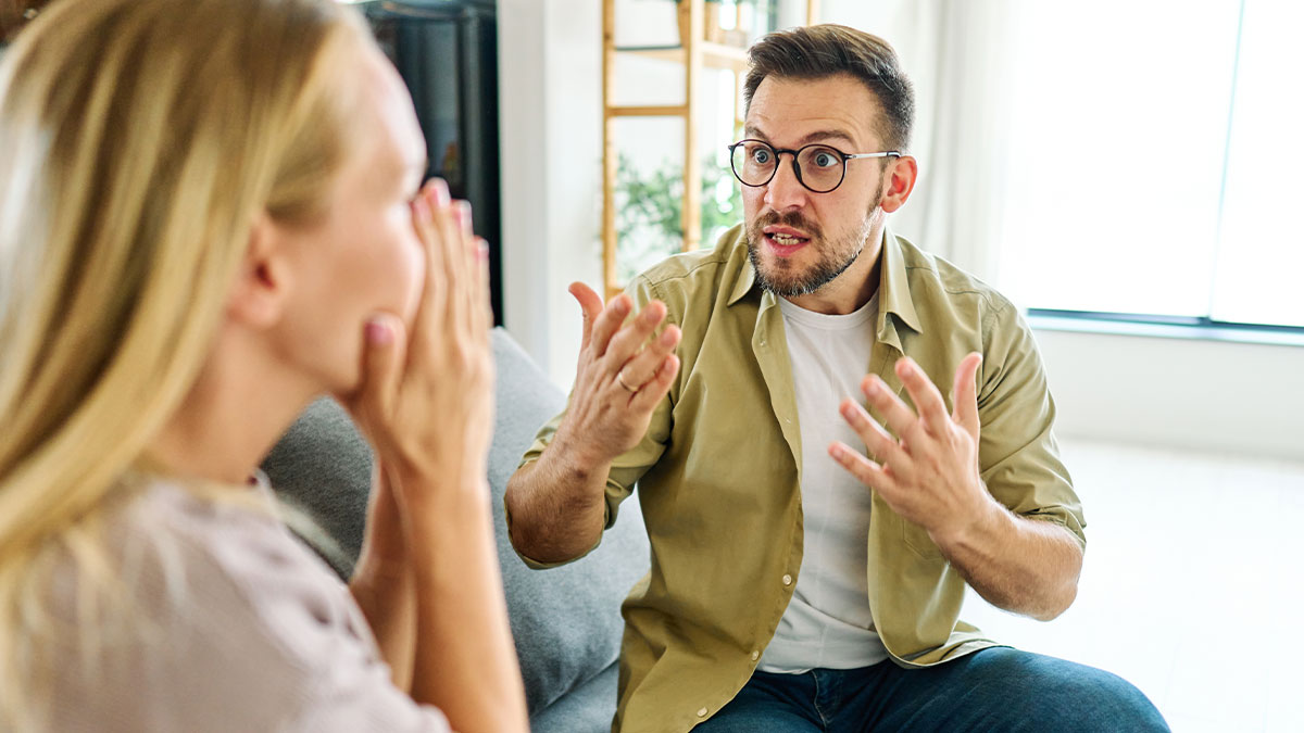 Man giving wife an ultimatum during emotional discussion about plastic surgery while seated in a living room.