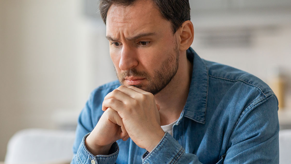 Man in a denim shirt looking worried and thoughtful, reflecting new mom struggles and husband judging silently.
