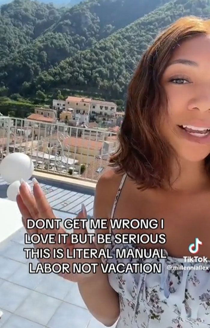 Woman in floral dress on balcony with mountain view sharing a TikTok screenshot about manual labor, smart content.