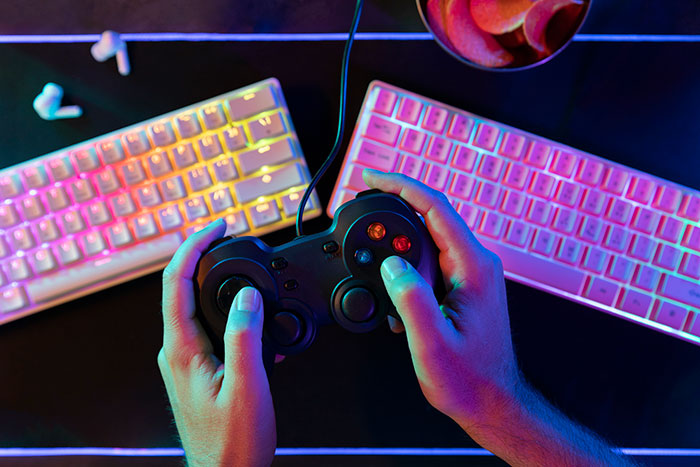 Person holding a game controller with colorful keyboards and a snack bowl under vibrant lighting for daily dose facts.