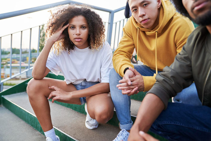 Three teens sitting on outdoor steps with serious expressions, reflecting tension over time with dad and ex issues.