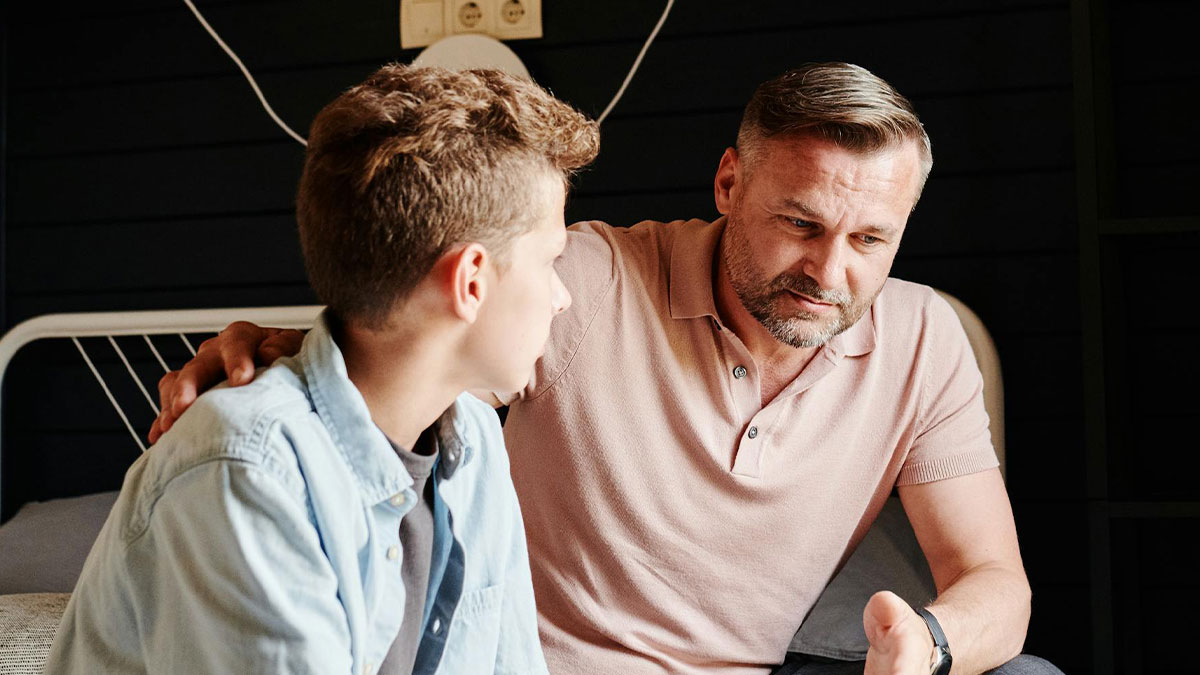 Dad looking irked while talking seriously to teen boy, reflecting family tension over Europe trip plans.