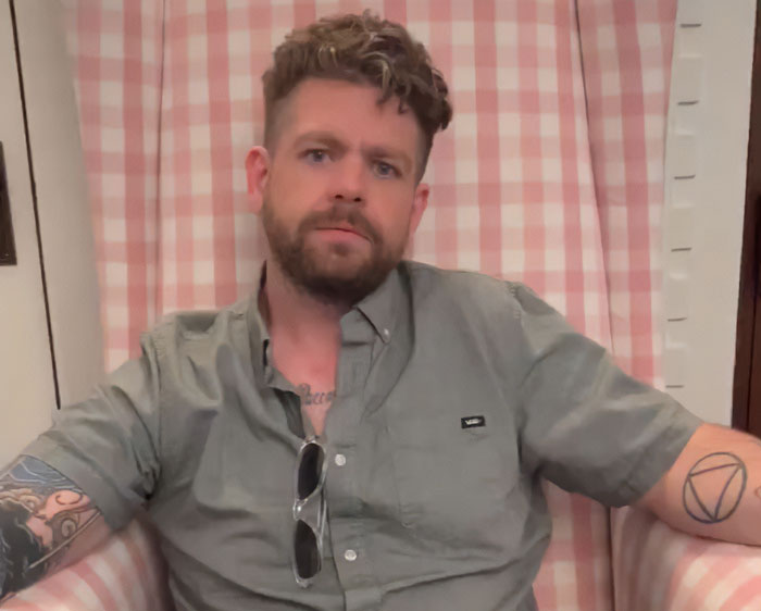 Man with tattoos and beard sitting in a chair, related to Roger Waters and Ozzy Osbourne son responding to criticism.