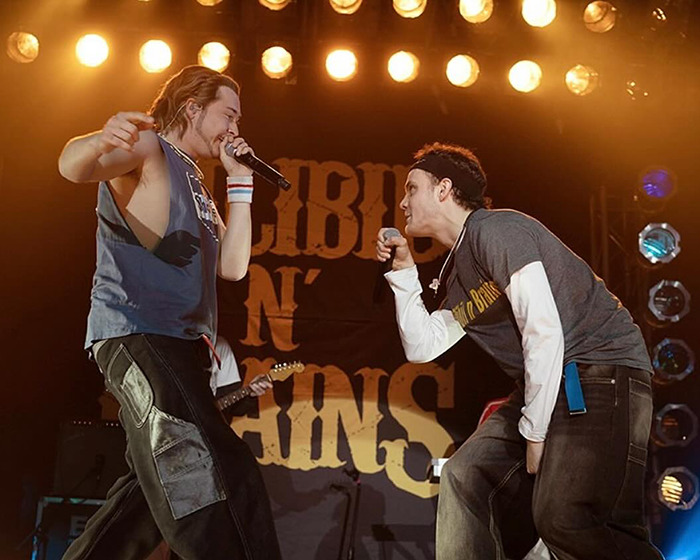 Two men performing energetically on stage during a music event with intense lighting and crowd engagement. Two men performing energetically on stage during a music event with intense lighting and crowd engagement.