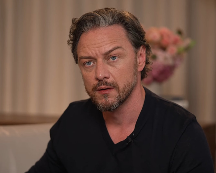 James McAvoy in a black shirt, seated indoors with a focused expression, during an interview setting. James McAvoy in a black shirt, seated indoors with a focused expression, during an interview setting.