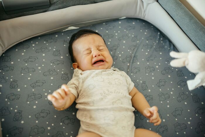 Crying baby lying on a patterned mat with toy nearby, illustrating emotional expression in daily life.