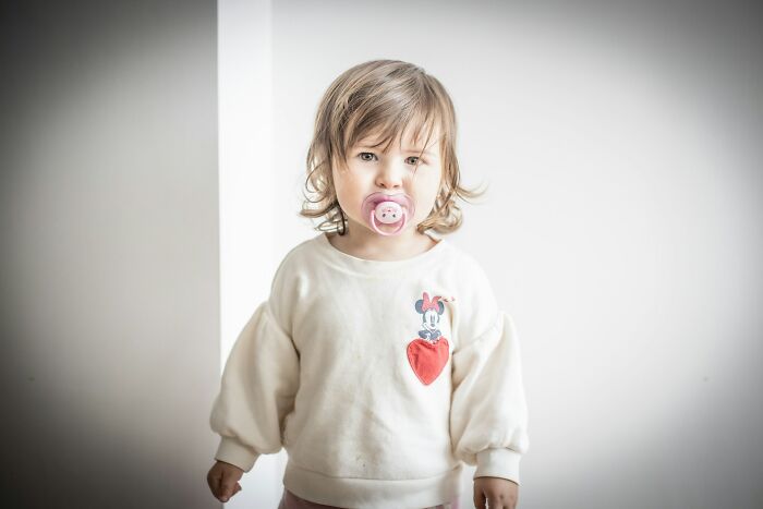 Young child with pacifier wearing a white sweatshirt with a heart and cartoon character, illustrating kaomojis concept.