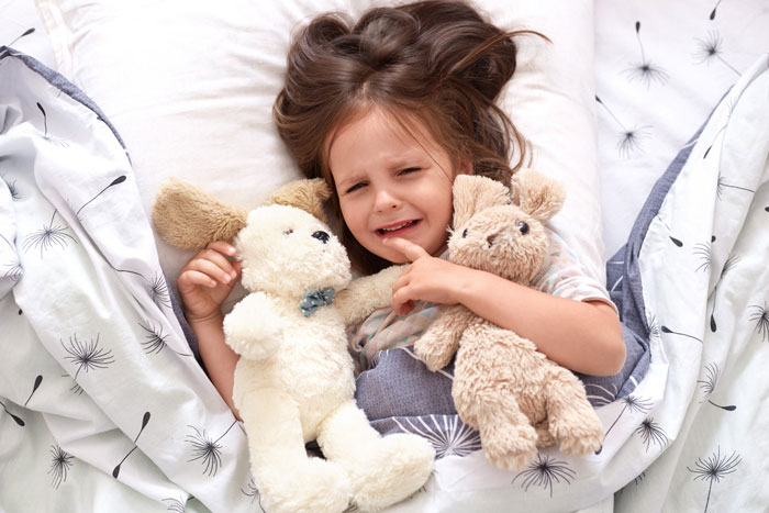 Young girl upset in bed holding stuffed animals, illustrating kid being kicked out of roommate’s bed conflict scenario. Young girl upset in bed holding stuffed animals, illustrating kid being kicked out of roommate’s bed conflict scenario.