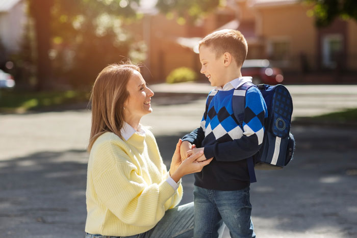 Mother kneeling and smiling at her son with a backpack at a kids bus stop, illustrating positive parenting moments. Mother kneeling and smiling at her son with a backpack at a kids bus stop, illustrating positive parenting moments.