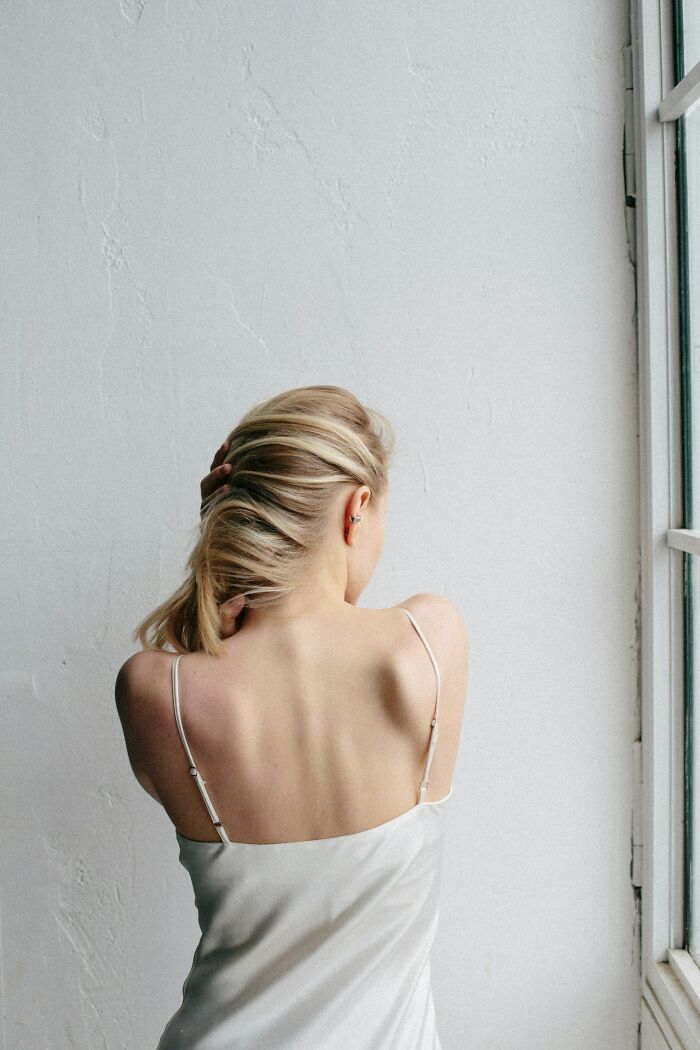 Woman in a white dress with exposed back near a window, representing tattoo clients considering designs from artists.