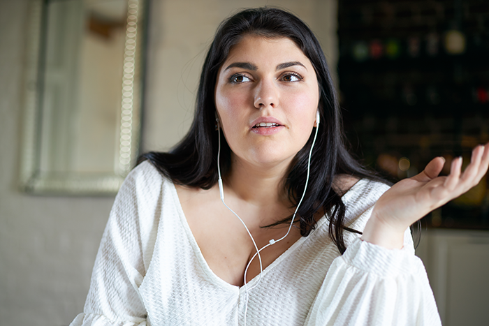 Woman wearing earphones, gesturing while discussing flight comfort and seating suggestions with a friend. Woman wearing earphones, gesturing while discussing flight comfort and seating suggestions with a friend.
