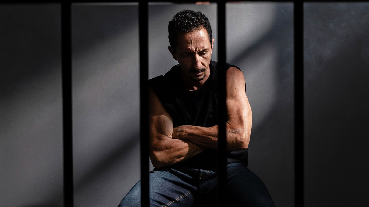 Man behind prison bars looking down with arms crossed, illustrating lawyers and cops discussing incrimination cases.