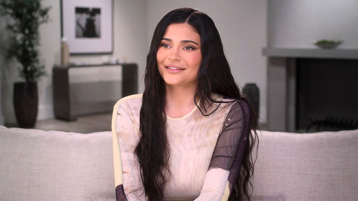 Young woman with long dark hair sitting on a couch, discussing kaomojis and cultural appropriation in a casual setting.