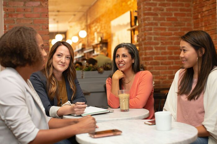 Four diverse women having a lively discussion at a cafe, sharing opinions on overhyped products and consumer trends.