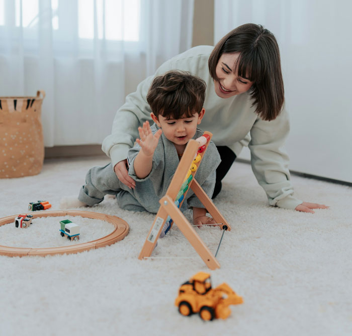 Live-in nanny playing with toddler on floor surrounded by toys in a bright room with white carpet and curtains. Live-in nanny playing with toddler on floor surrounded by toys in a bright room with white carpet and curtains.