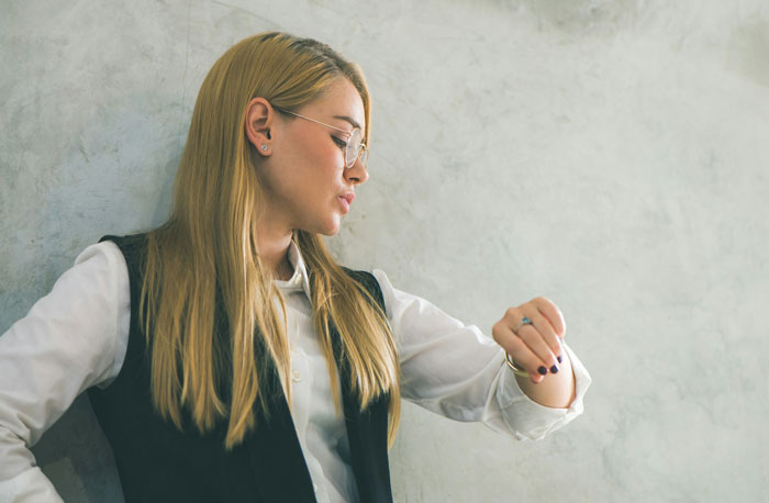 Young live-in nanny in a vest and glasses looking at her watch, reflecting on curfew set by mom on nights off Young live-in nanny in a vest and glasses looking at her watch, reflecting on curfew set by mom on nights off