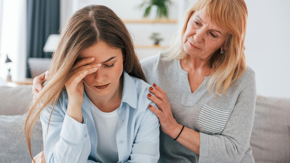Pregnant daughter-in-law upset on couch while mother-in-law tries to comfort her in a tense family moment.