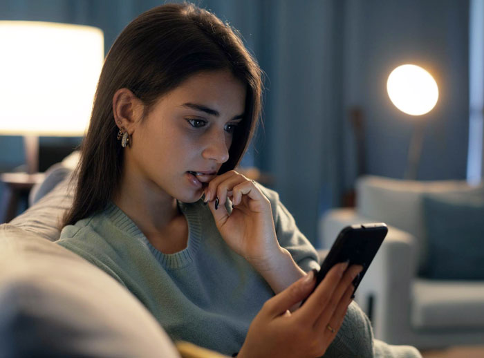 Young woman looking worried while scrolling on her phone at home, concerned about online date's behavior and posts memory