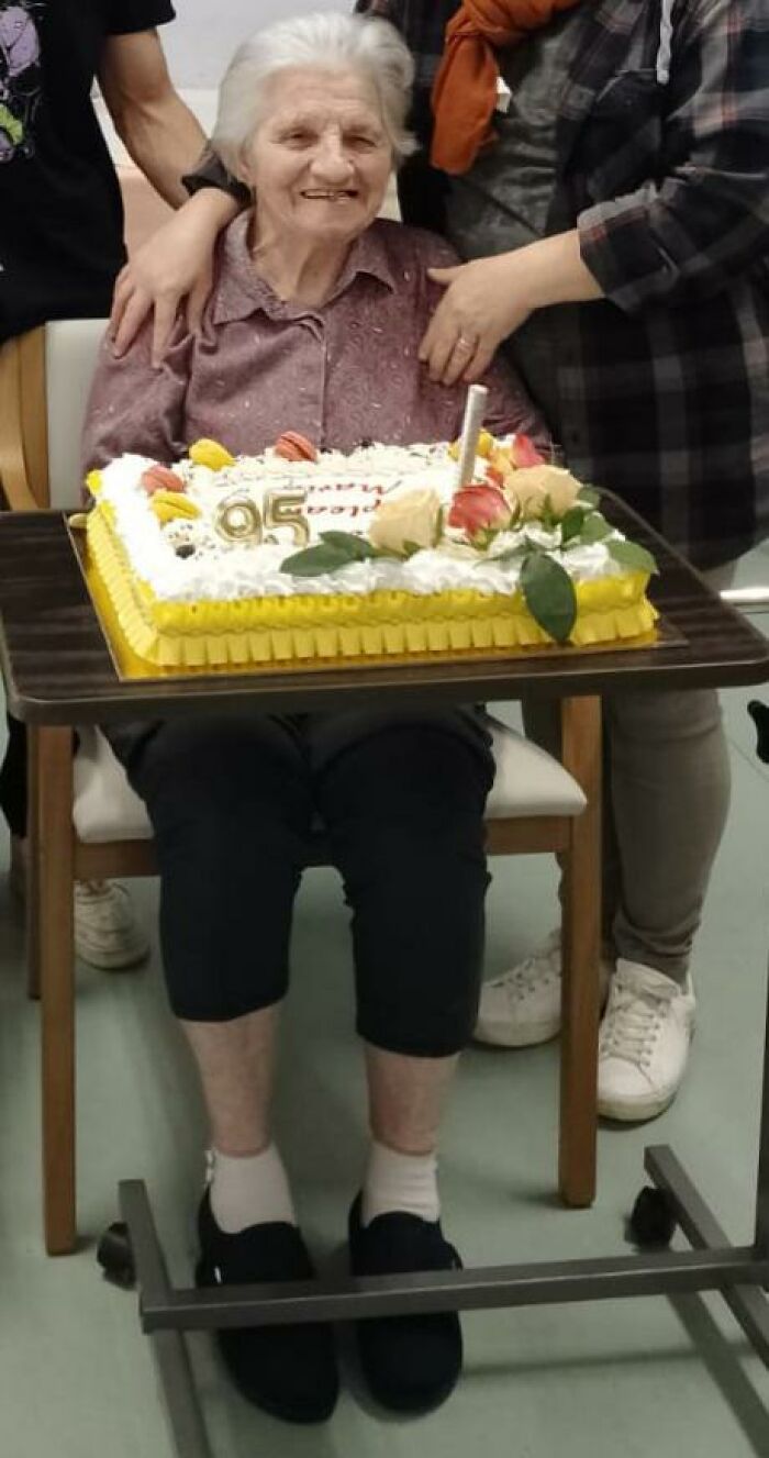 Elderly mom smiling with family around her, celebrating a 95th birthday with a decorated cake, showing wholesome happiness.