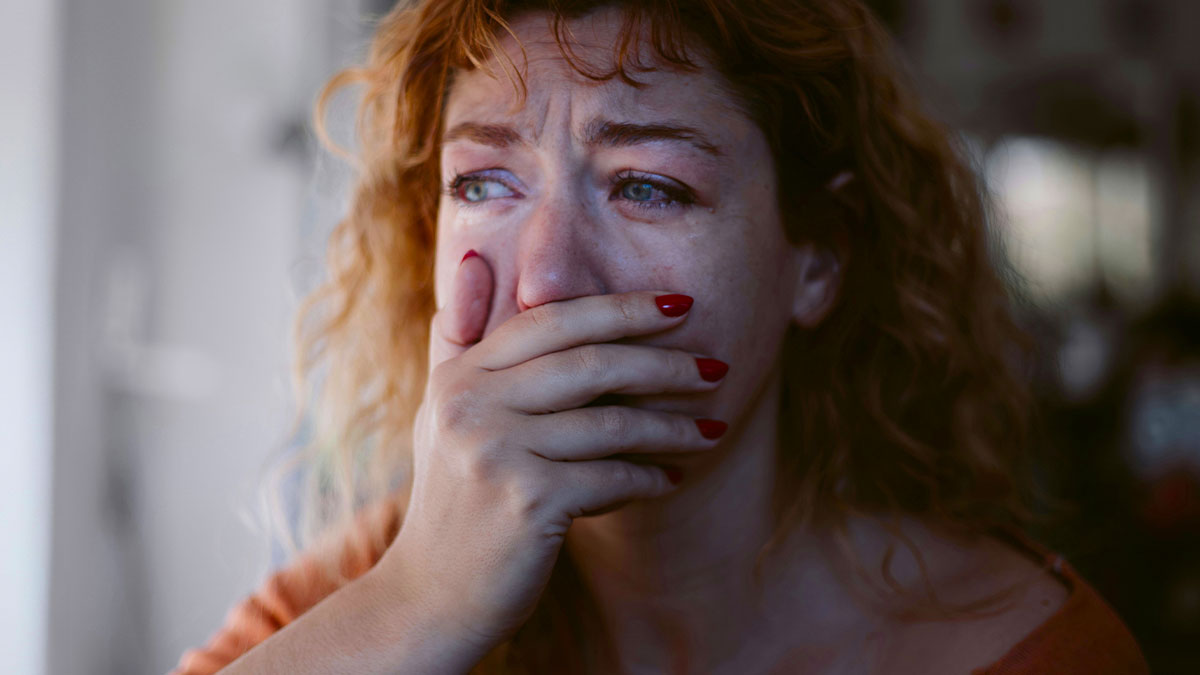 Pregnant woman looks distressed and upset, covering her mouth with her hand in an emotional moment at home.