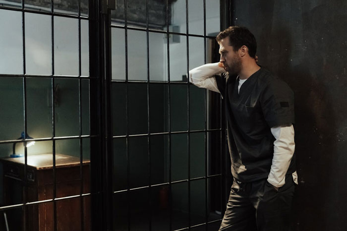 Man standing behind prison bars, looking distressed and bearing consequences despite being proven not guilty of a crime. Man standing behind prison bars, looking distressed and bearing consequences despite being proven not guilty of a crime.