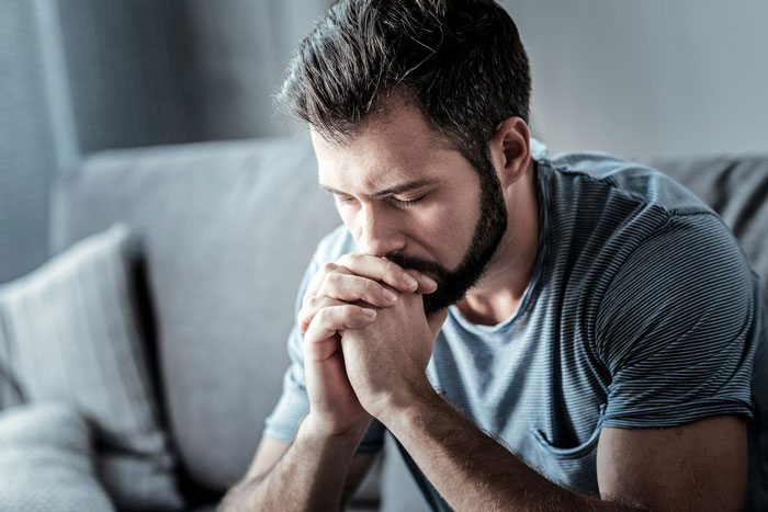 Man with beard sitting on couch, deep in thought and concern, illustrating consequences despite proven not guilty of a crime Man with beard sitting on couch, deep in thought and concern, illustrating consequences despite proven not guilty of a crime