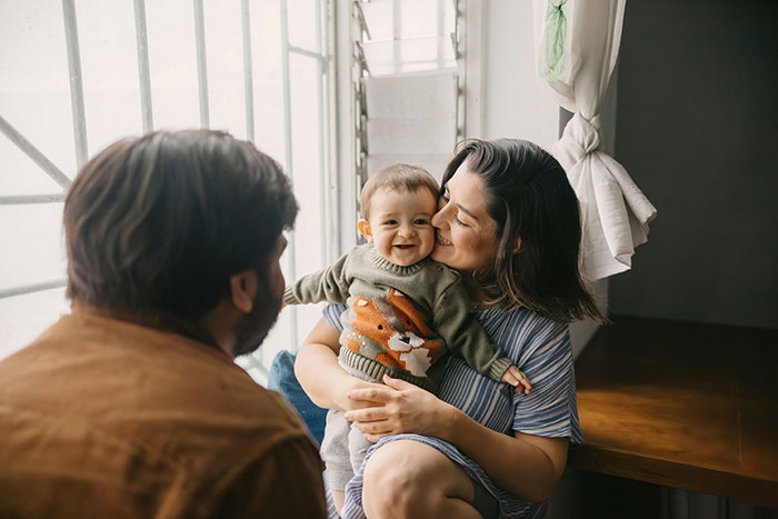 Mother holding baby smiling at man by window, illustrating robotically calculated choice based on brains over heart. Mother holding baby smiling at man by window, illustrating robotically calculated choice based on brains over heart.