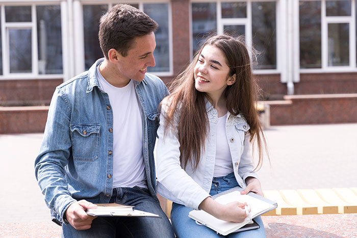Young couple sitting outdoors with notebooks, discussing an art class memory disagreement between them. Young couple sitting outdoors with notebooks, discussing an art class memory disagreement between them.