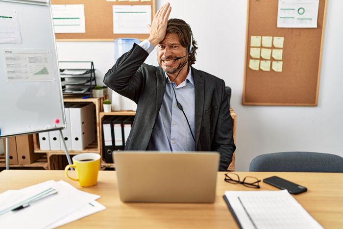 Man in business suit with headset frustrated at laptop, illustrating employees maliciously complying with dress code.
