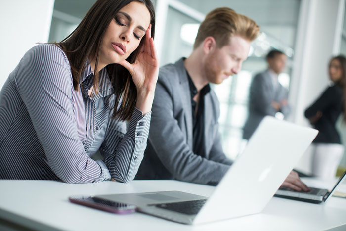 Stressed employees sitting at desks in office, showing frustration with manager’s overly strict dress code policy.