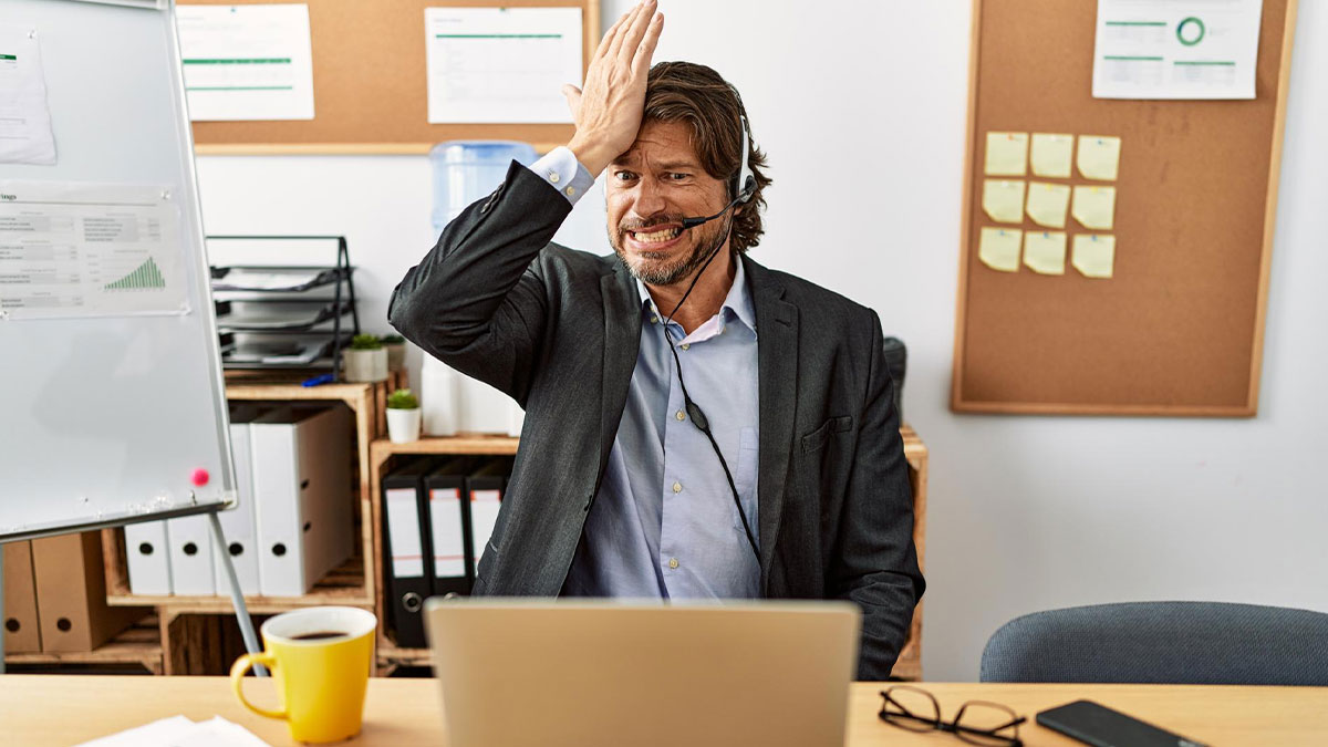 Frustrated employee in office with headset reacting to strict dress code policy during virtual meeting.