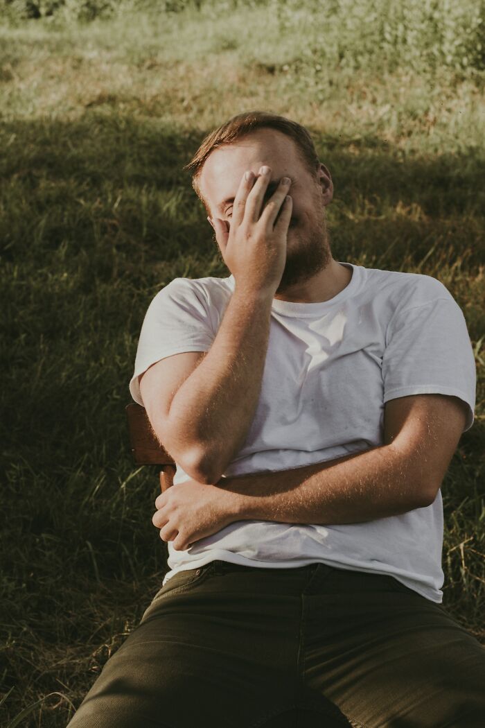 Man sitting on a chair outdoors, covering his face with his hand, reflecting regret over the worst things clients wanted tattooed.