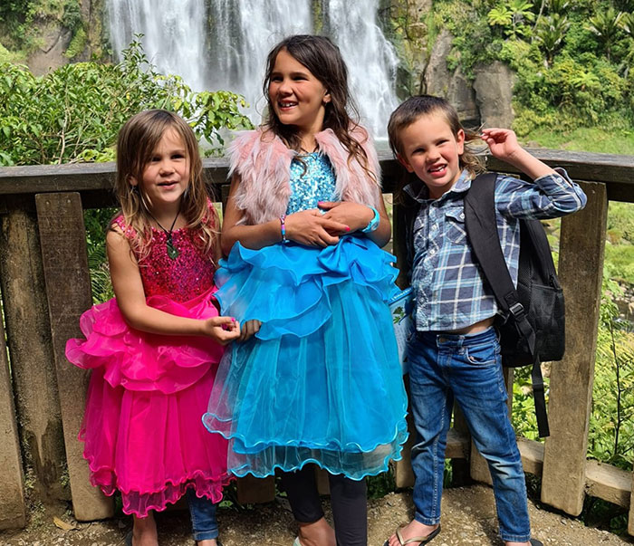 Three kids in colorful dresses and casual clothes posing by a wooden fence near a waterfall, related to vanished wilderness case. Three kids in colorful dresses and casual clothes posing by a wooden fence near a waterfall, related to vanished wilderness case.