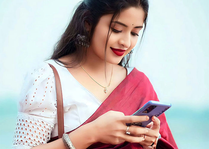 Woman in a red saree with delicate jewelry pretending to be the bride at SIL’s wedding while using her phone outdoors. Woman in a red saree with delicate jewelry pretending to be the bride at SIL’s wedding while using her phone outdoors.