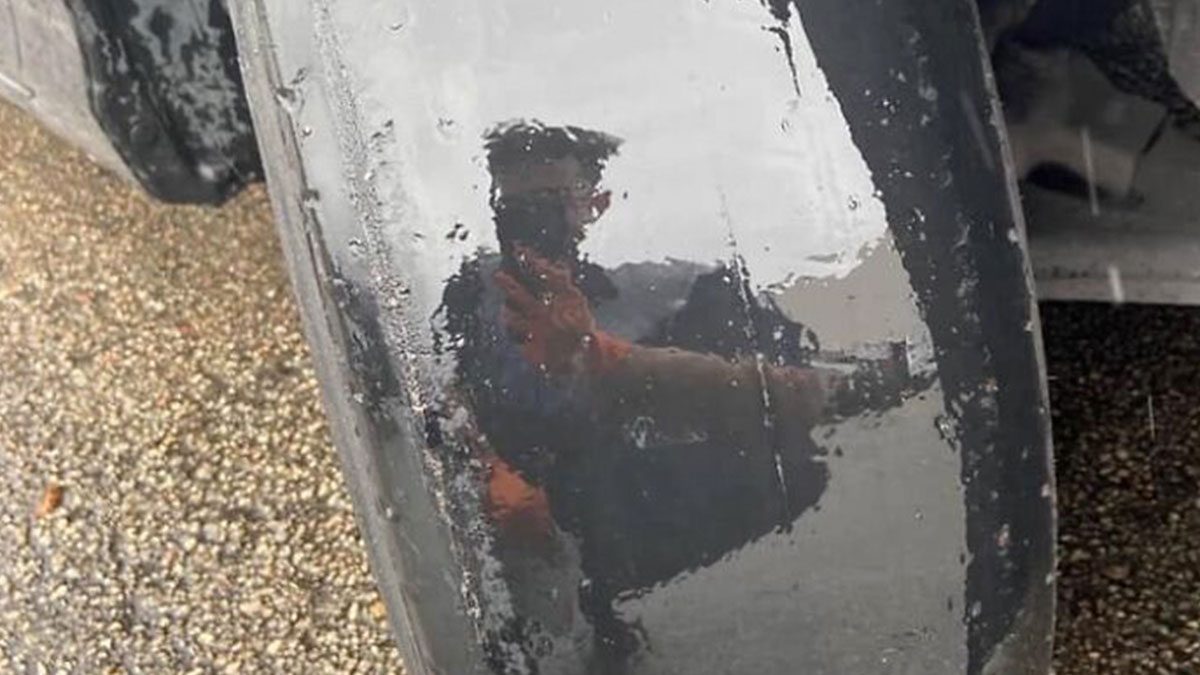Reflection of a person taking a photo of a severely worn car tire, highlighting a mechanic's unusual finds.