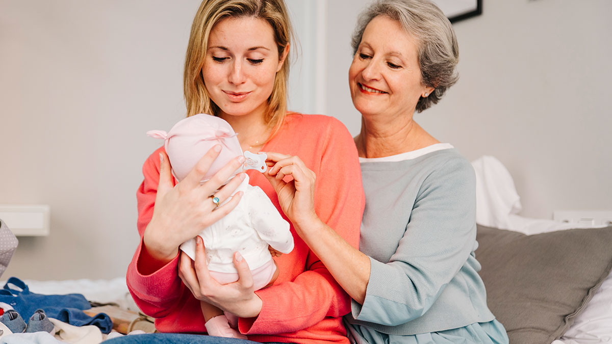 Mother and mother-in-law sharing a moment as they secretly plan to see the newborn baby, new mom looking surprised.