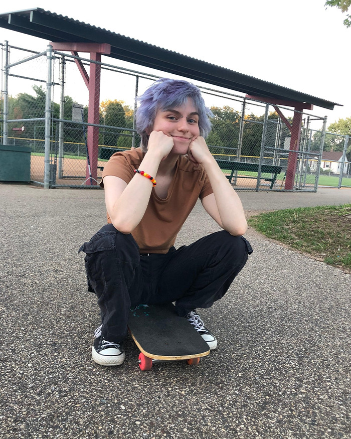 Young person with purple hair sitting on a skateboard at a park, linked to Minneapolis suspect furry girlfriend report Young person with purple hair sitting on a skateboard at a park, linked to Minneapolis suspect furry girlfriend report
