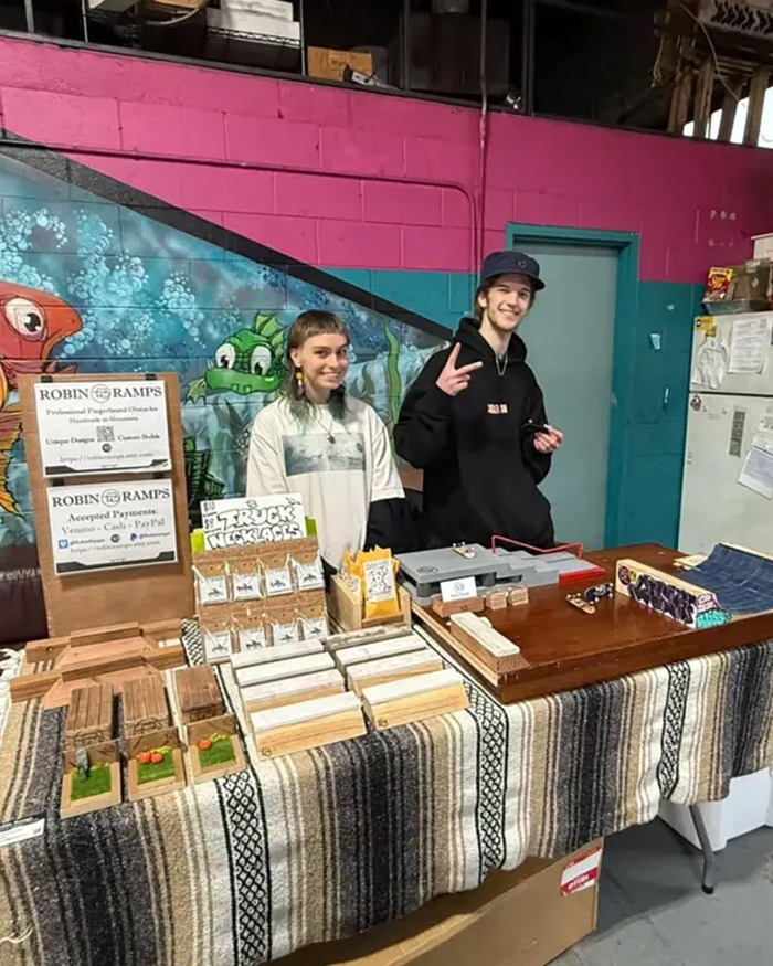Two people standing behind a table with handmade crafts at a Minneapolis event, related to furry community. Two people standing behind a table with handmade crafts at a Minneapolis event, related to furry community.