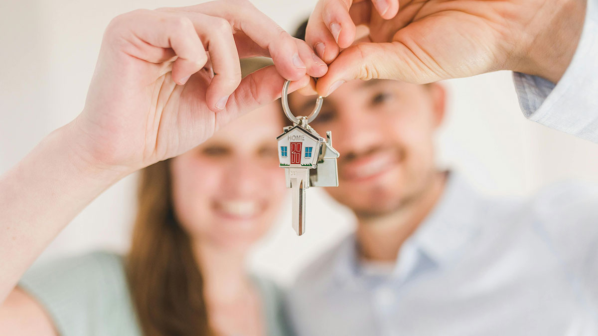 Close-up of a smiling couple holding a house key with a keychain, symbolizing subtle ways women notice misogyny.