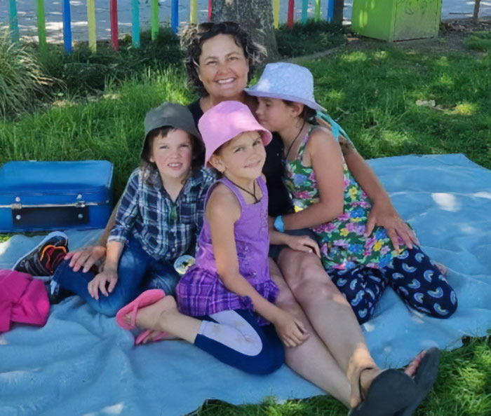 Mom with kids who vanished in wilderness sitting on blanket outdoors near colorful fence and picnic items Mom with kids who vanished in wilderness sitting on blanket outdoors near colorful fence and picnic items