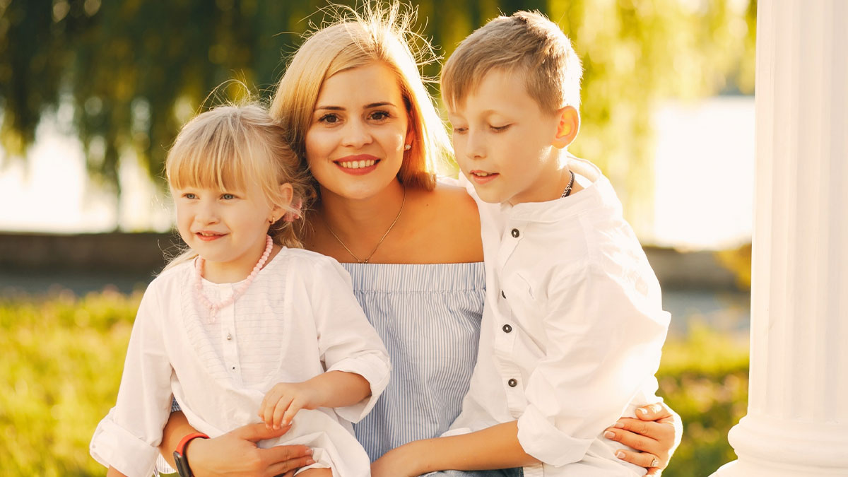 Young mother smiling outdoors with two children, highlighting family and caregiving challenges involving disabled daughter care.