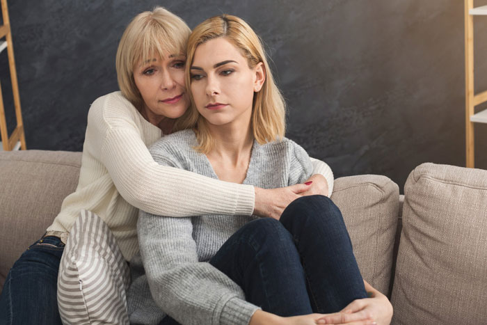 Older woman hugging younger woman on couch, showing support and care in a mom retirement plan context. Older woman hugging younger woman on couch, showing support and care in a mom retirement plan context.