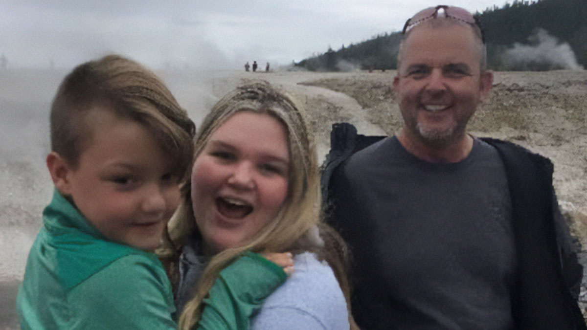 Family photo at an outdoor location with a young boy, woman, and man smiling amidst a misty background.